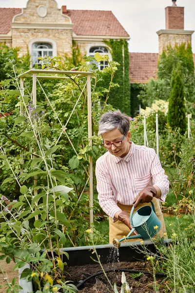 Attraktive, fröhliche reife Frau mit stylischen Gläsern, die Pflanzen in ihrem Garten in England gießt — Stockfoto