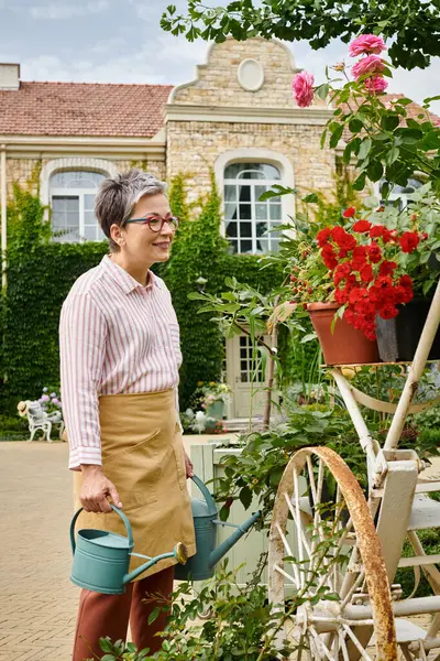 Красивая, веселая, зрелая женщина поливает свои яркие цветы в своем саду в Англии — стоковое фото