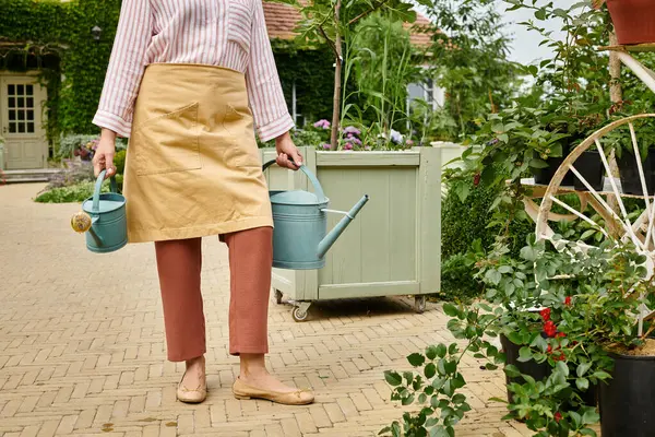 Обрезанный вид зрелой женщины, держащей две банки с водой рядом с растениями перед ее домом в Англии — стоковое фото