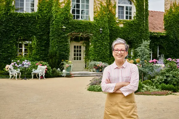 Beautiful jolly mature woman with glasses in cozy attire looking at camera near her house in England — Stock Photo