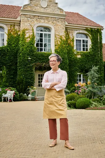 Good looking jolly mature woman with glasses posing near her house in England and looking away — Stock Photo