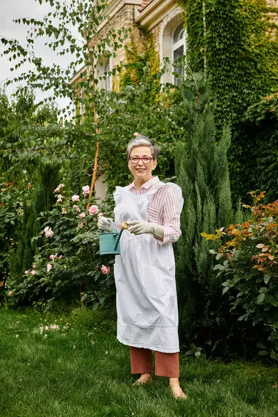 Attractive mature jolly woman with glasses holding watering can and smiling happily at camera — Stock Photo