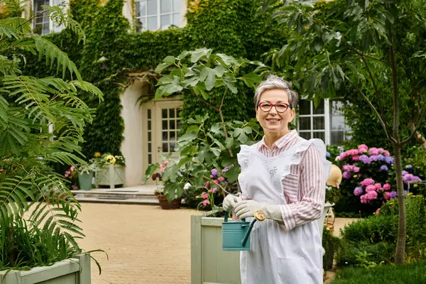 Attractive mature jolly woman with glasses holding watering can and smiling happily at camera — Stock Photo