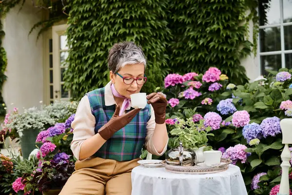 Good looking jolly mature woman drinking hot tea at breakfast in garden of her house in England — Stock Photo
