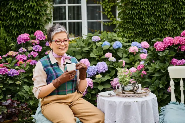 Good looking jolly mature woman drinking hot tea at breakfast in garden of her house in England — Stock Photo