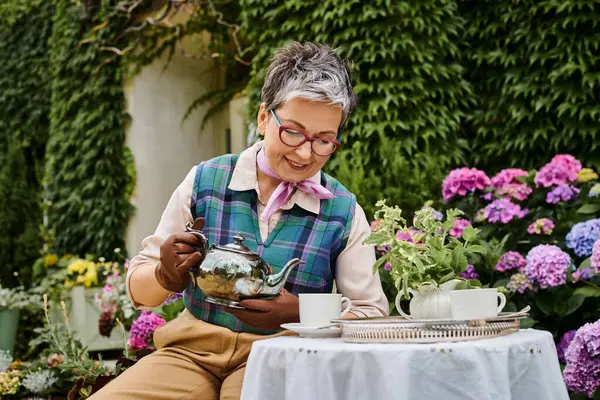 Good looking merry mature woman drinking hot tea at breakfast in garden of her house in England — Stock Photo