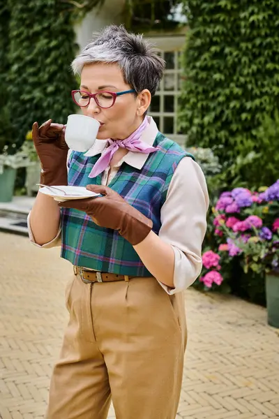 Attractive joyful mature woman drinking hot tea at breakfast in garden of her house in England — Stock Photo