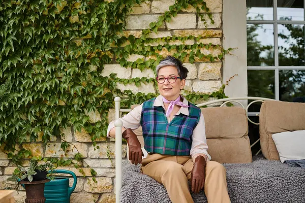 Atraente alegre mulher madura sentado no sofá perto de sua casa na Inglaterra e olhando para a câmera — Fotografia de Stock