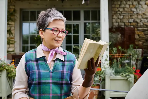 Сложная зрелая радостная женщина в очках, читающая книгу возле своего дома в сельской Англии — стоковое фото