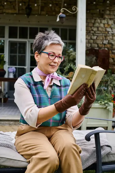 Sophisticated mature joyous woman with glasses reading book near her house in rural England — Stock Photo