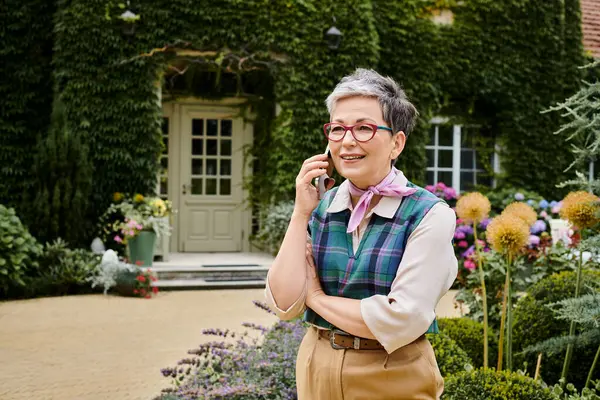 Elegant cheerful mature woman with stylish glasses talking by phone net to her house in England — Stock Photo
