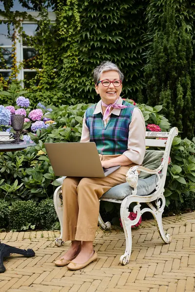 Debonair reife fröhliche Frau in schicker Kleidung sitzt mit Laptop zur Teezeit in der Nähe ihres Hauses in England — Stockfoto