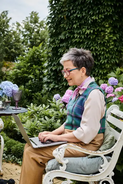 Debonair mature merry woman in chic attire sitting with laptop at tea time near her house in England — Stock Photo