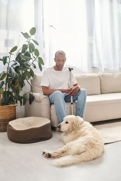 Homme afro-américain handicapé avec myasthénie gravis assis à côté de son chien Labrador fidèle sur un canapé confortable à la maison. — Photo de stock