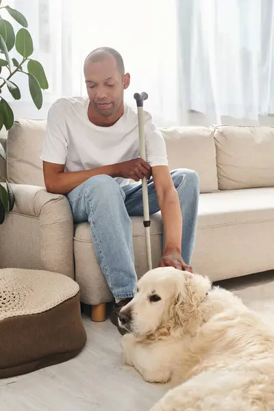 Un uomo afroamericano con miastenia gravis seduto comodamente su un divano accanto al suo fedele cane Labrador. — Foto stock