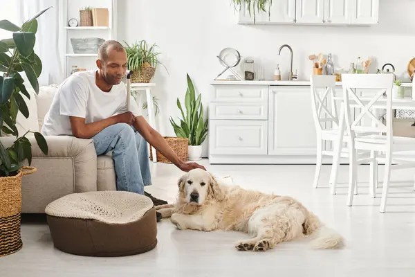 Un uomo afroamericano con miastenia gravis siede accanto al suo cane Labrador sul divano di casa. — Foto stock