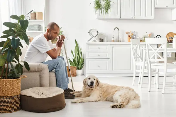 Инвалид афроамериканец с миастенией Гравис сидит на диване рядом со своей лояльной собакой-лабрадором, демонстрируя разнообразие и включенность. — стоковое фото