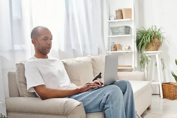 Афроамериканец с миастенией сидит на диване, используя ноутбук — стоковое фото