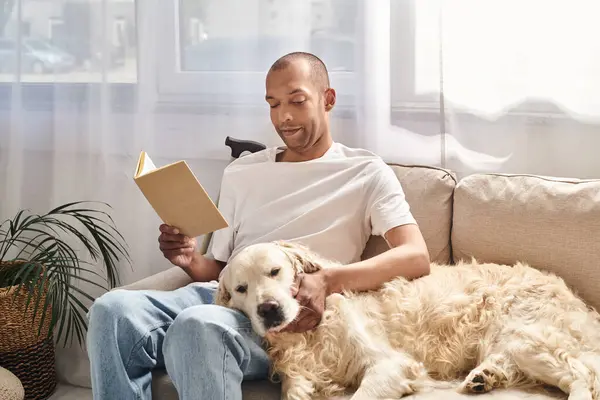 Un Afro-Américain handicapé se détend sur un canapé, lisant un livre aux côtés de son fidèle chien du Labrador. Ils semblent tous deux perdus dans le monde de la parole écrite. — Photo de stock