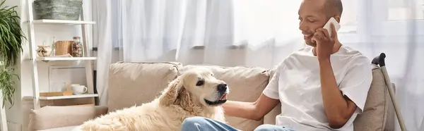 Un uomo con miastenia gravis siede su un divano a parlare su un cellulare accanto al suo fedele cane Labrador. — Foto stock