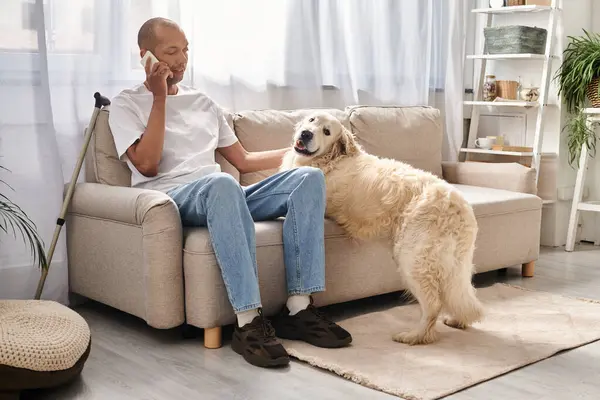 An African American man sits on a couch, talking on a cell phone next to his loyal Labrador dog at home. — Stock Photo