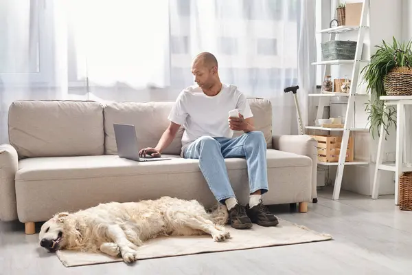 Un hombre afroamericano, viviendo con miastenia gravis, se sienta con su leal perro Labrador en un acogedor sofá en casa. - foto de stock