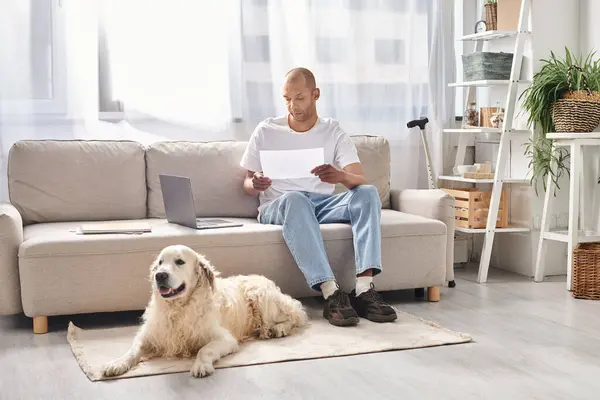Інвалідний афроамериканський чоловік з міастенією сидить на дивані поруч зі своїм собакою-лабрадором вдома, підкреслюючи різноманітність і включення. — стокове фото