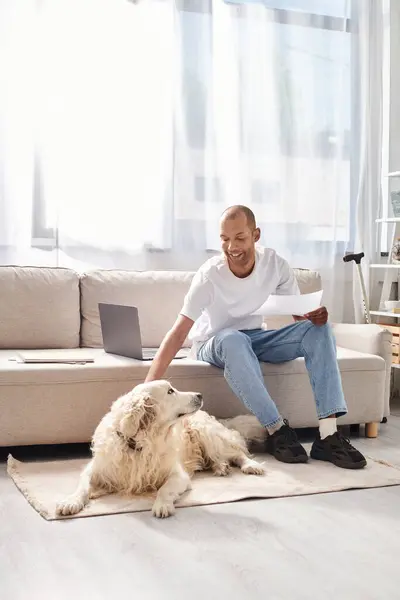 An African American man with myasthenia gravis sitting on a couch next to his loyal Labrador dog at home. — Stock Photo