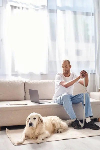 Un uomo afroamericano disabile si rilassa accanto al suo fedele cane Labrador su un comodo divano, abbracciando la diversità e l'inclusione. — Foto stock
