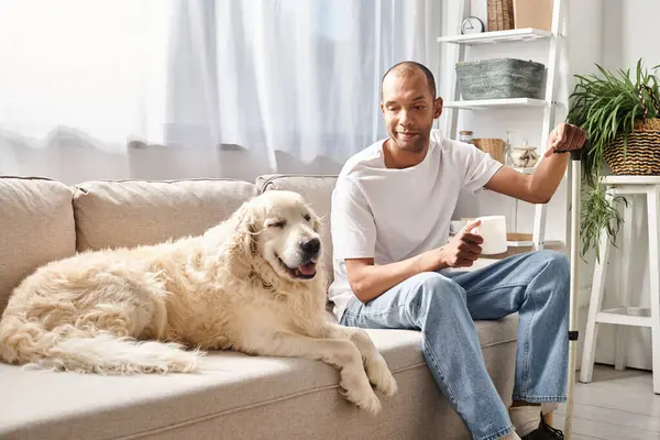 Un uomo afroamericano disabile con miastenia gravis siede su un divano coccolato con il suo cane Labrador, mostrando diversità e inclusione.. — Foto stock