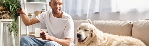 Инвалид афроамериканец с миастенией Гравис расслабляется на диване рядом со своей лояльной собакой-лабрадором, подчеркивая разнообразие и включенность. — стоковое фото