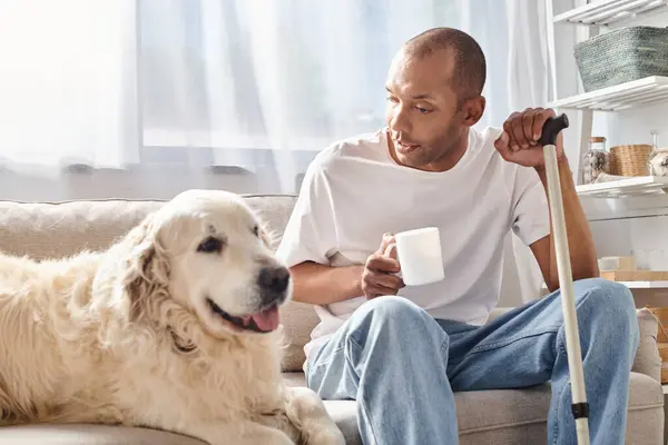 Чоловік з міастенією гравіс сидить на дивані, насолоджуючись компанією зі своїм вірним собакою Лабрадором у затишній обстановці у вітальні. — стокове фото