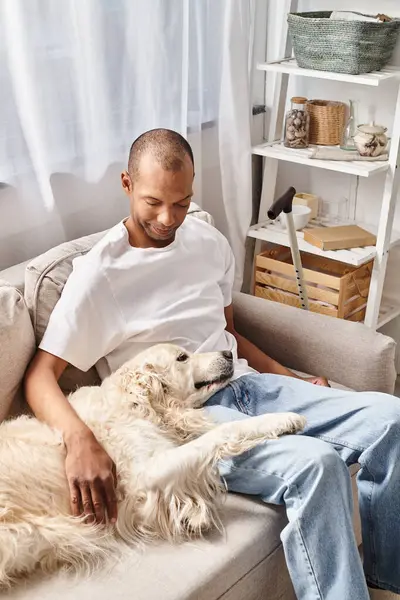 Um homem com miastenia gravis relaxando em um sofá com seu cão Labrador, mostrando diversidade e inclusão. — Fotografia de Stock