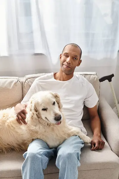 Un uomo afroamericano con miastenia grave si rilassa su un divano a casa con il suo fedele cane Labrador al suo fianco. — Foto stock