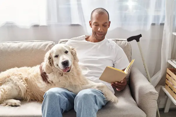 A man with myasthenia gravis relaxes at home on a couch with his loyal Labrador dog, engrossed in a good book. — Stock Photo