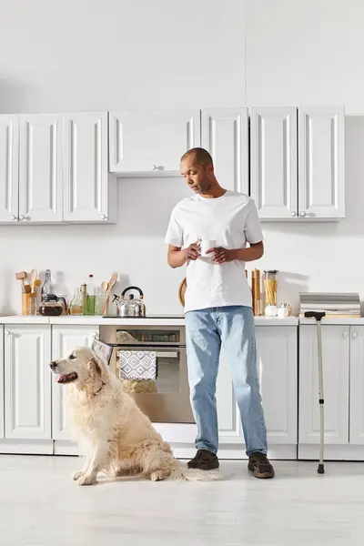 A disabled African American man with myasthenia gravis stands in a kitchen alongside his loyal Labrador dog. — Stock Photo