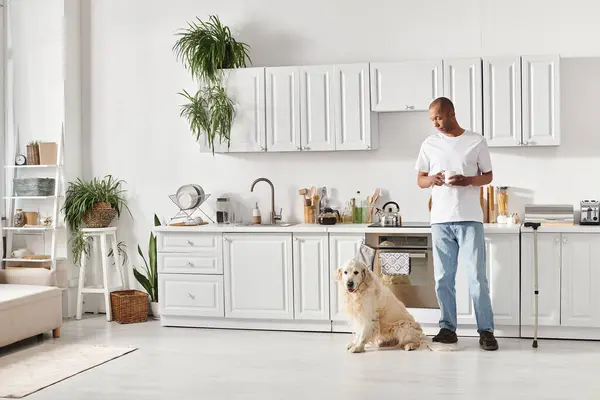 Афроамериканец с миастенией гравис стоит на кухне с лабрадором, демонстрируя разнообразие и включение. — стоковое фото