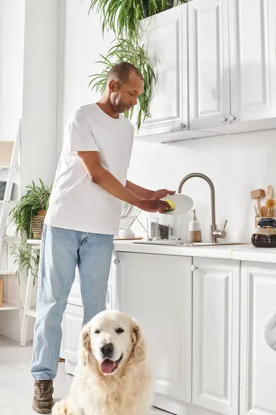 An African American man standing in a kitchen next to his Labrador dog. — Stock Photo