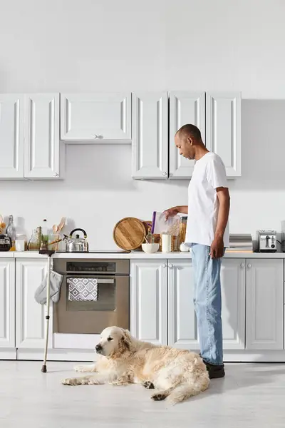 Афроамериканец с миастенией и грависом стоит рядом со своей верной собакой-лабрадором в уютной кухне. — стоковое фото