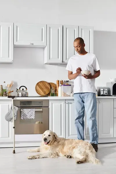 Инвалид афроамериканец с миастенией и грависом стоит на кухне рядом со своей верной собакой-лабрадором. — стоковое фото