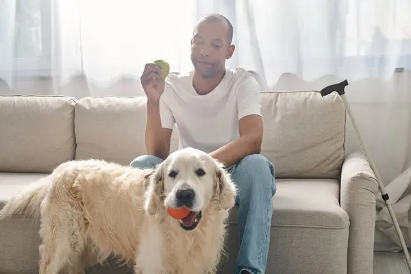 Um afro-americano deficiente sentado em um sofá ao lado de seu cão Labrador leal, mostrando diversidade e inclusão. — Fotografia de Stock