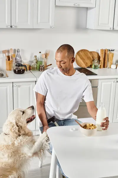 Ein behinderter Afroamerikaner sitzt an einem Küchentisch und genießt die Gesellschaft seines treuen Labrador-Hundes. — Stockfoto