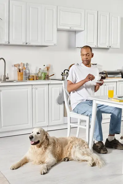 Un uomo afroamericano disabile seduto a un tavolo da cucina con il suo fedele cane Labrador al suo fianco. — Foto stock