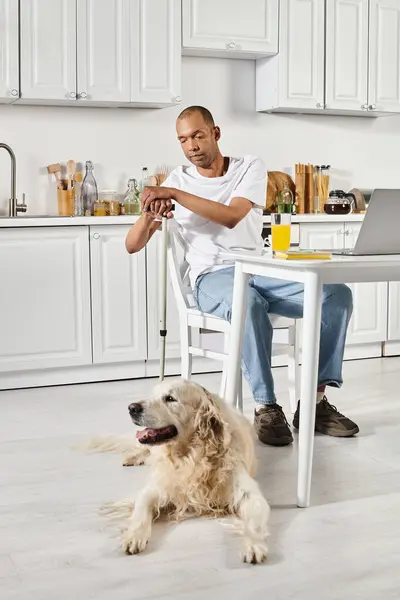 A disabled African American man sits at a table with a Labrador dog in front of him, displaying diversity and inclusion. — Stock Photo