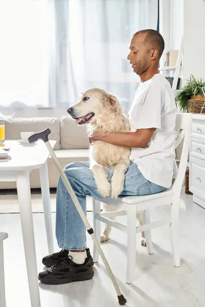 An African American man, sitting in a chair, is tenderly holding his Labrador dog in a heartwarming display of love and connection. — Stock Photo