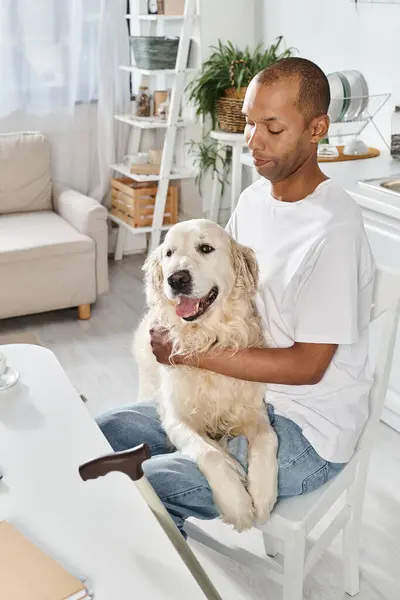 A disabled African American man sits contemplatively in a chair, holding his loyal Labrador dog beside him. — Stock Photo