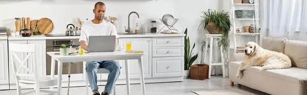 Un Afro-Américain handicapé assis à une table, concentré sur son ordinateur portable, tandis que son compagnon du Labrador est assis à ses côtés. — Photo de stock