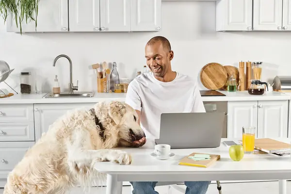 A disabled African American man sits at a table with a laptop, accompanied by his loyal Labrador retriever. — Stock Photo