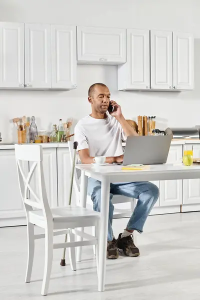 Ein behinderter afroamerikanischer Mann mit Myasthenia-Gravis-Syndrom sitzt an einem Küchentisch und ist tief in ein Telefonat verwickelt. — Stockfoto