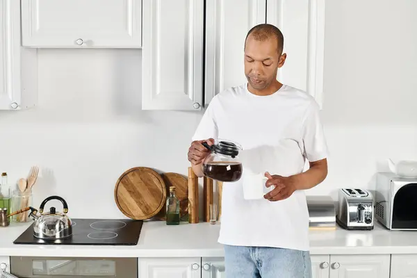 Ein behinderter Afroamerikaner mit Myasthenia-Gravis-Syndrom steht in einer Küche und hält eine Kaffeekanne in der Hand.. — Stockfoto
